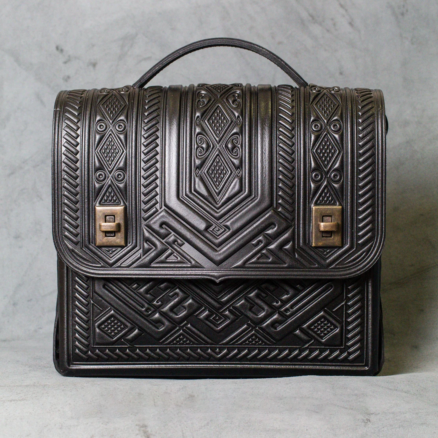 Deep Black Embossed Tribal Geometric Structured Rectangular Satchel With Curved Fixed Top Handle, Punch-Hole Shoulder Strap And Dual Antique Brass Turn-Lock Flap Fastener Hardware Leather Bag